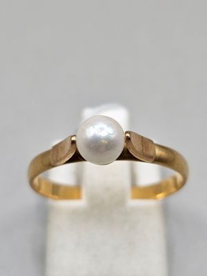 un gros plan d'une bague en or sertie d'une perle blanche