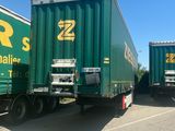 two green semi trailers that are parked on the side of the road