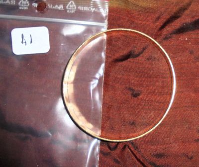 une photo d'un bracelet rigide en or posé sur un tissu rouge