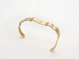 un gros plan d'un bracelet manchette en or sur fond blanc