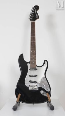 Une guitare électrique est posée sur un support, sur une surface blanche.
