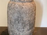un vase en pierre posé sur une table, avec un mur blanc en arrière-plan