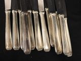 six silverplated knives are lined up in a row on a black surface
