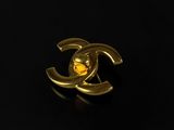 a close up of a gold chanel broocher on a black surface
