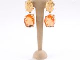 une paire de boucles d'oreilles ornées de pierres orange, présentées sur un support, sur fond blanc