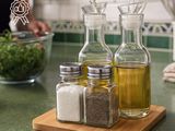 bottles of oil, salt, and pepper on a cutting board with a person in the background