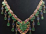 a gold necklace with green and purple stones on a mannequin