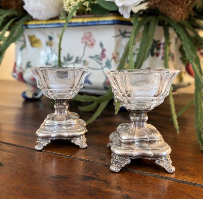 deux bougeoirs en verre posés sur une table, avec des fleurs en arrière-plan