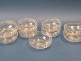 six clear glass cups with gold rims on a blue surface