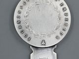 a silver spoon with a silver plate on it that has a wreath on it