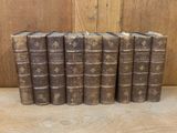 six old books lined up in a row on a wooden surface