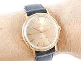 a gold watch on a woman ' s wrist with a black strap