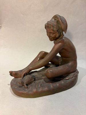 bronze statue of a boy sitting on a rock with his feet crossed