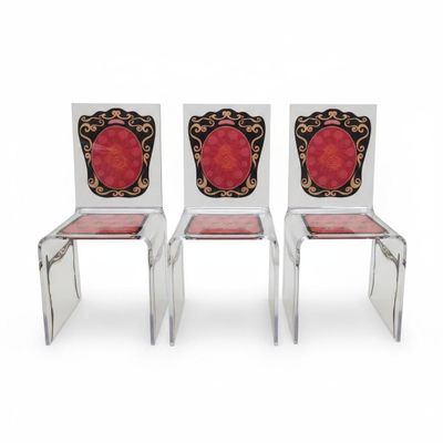 une paire de chaises transparentes ornées de motifs rouges et dorés