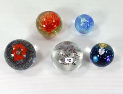 Quatre billes de verre sont posées sur une surface blanche, avec une fleur rouge au centre.