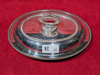 un plat en argent muni d'un couvercle en verre, posé sur un support rouge