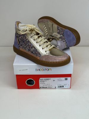 des baskets violettes et argentées pailletées posées sur une boîte, sur une surface blanche