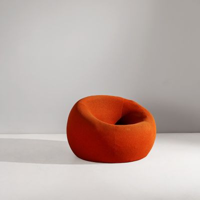 une chaise orange posée sur un sol blanc, à côté d'un mur blanc