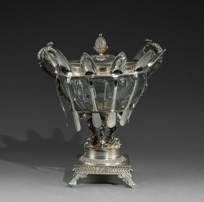 un vase ancien en métal argenté, accompagné de cuillères posées sur un socle