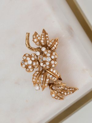 an image of a gold and diamond flower broochle on a white surface