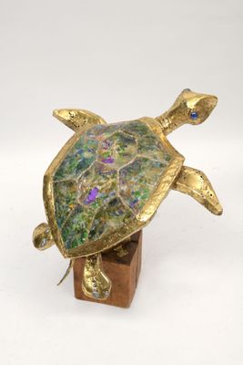 brass turtle figurine with multicolored glass eyes on a wooden base