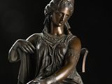 bronze statue of a woman sitting on a chair with a book in her lap
