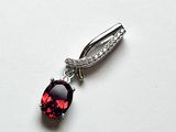 une image représentant un pendentif composé d'une pierre rouge et d'un diamant, posé sur une surface blanche