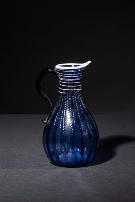 a blue glass pitcher with a black handle on a table