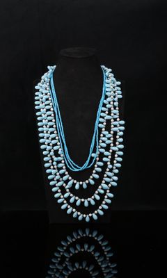 Un collier composé de perles de turquoise et de perles de nacre est présenté sur un mannequin