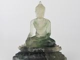 une statue de Bouddha en jade vert, assise sur un rocher, sur fond blanc