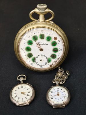 Trois types différents de montres de poche sont exposés sur un fond noir