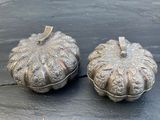 une paire de citrouilles en métal argenté posées sur une surface noire