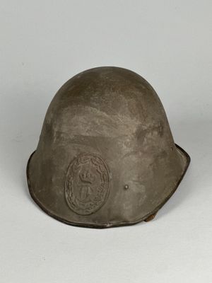 Un vieux casque repose sur une surface blanche, devant un fond blanc.
