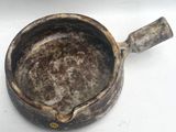 un petit pot marron muni d'une anse, posé sur une surface blanche