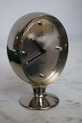 une horloge en argent posée sur une table en marbre