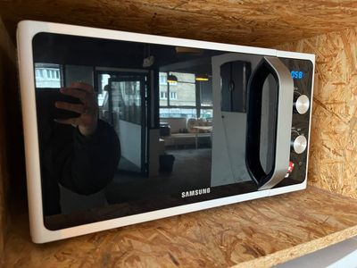 someone taking a picture of a microwave on a shelf in a kitchen