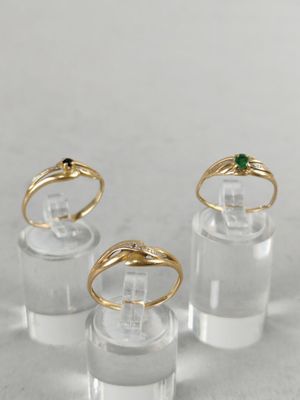 three gold and emerald rings sitting on top of a clear glass
