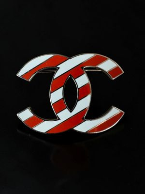 a red and white striped chanel logo pin on a black background