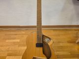 une guitare posée sur un support devant un mur, avec des guitares en arrière-plan