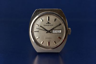 a close up of a silver watch on a blue surface