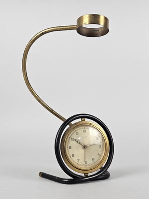 une image représentant une horloge posée sur un socle et surmontée d'une lampe
