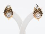 une paire de boucles d'oreilles en or et diamants posée sur un socle blanc