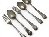 five silver spoons and a fork on a white surface