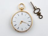 une montre de poche en or et une clé posées sur une surface blanche