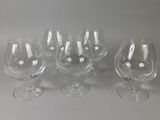 six verres à vin vides sont alignés sur une surface blanche