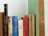 several books are stacked on a shelf with a clock on top of them
