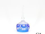 un petit vase en verre bleu muni d'une anse, posé sur une surface blanche