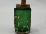a green glass bottle with a gold lid on a white surface