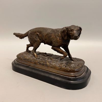statue en bronze représentant un chien en train de courir, posée sur un socle, sur fond blanc