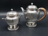 two silver teapots with wooden handles on a black surface